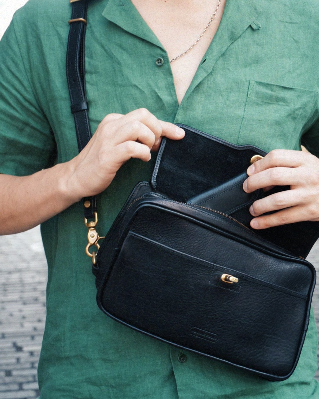 Black leather crossbosy bag with clasp and zip, being opened.