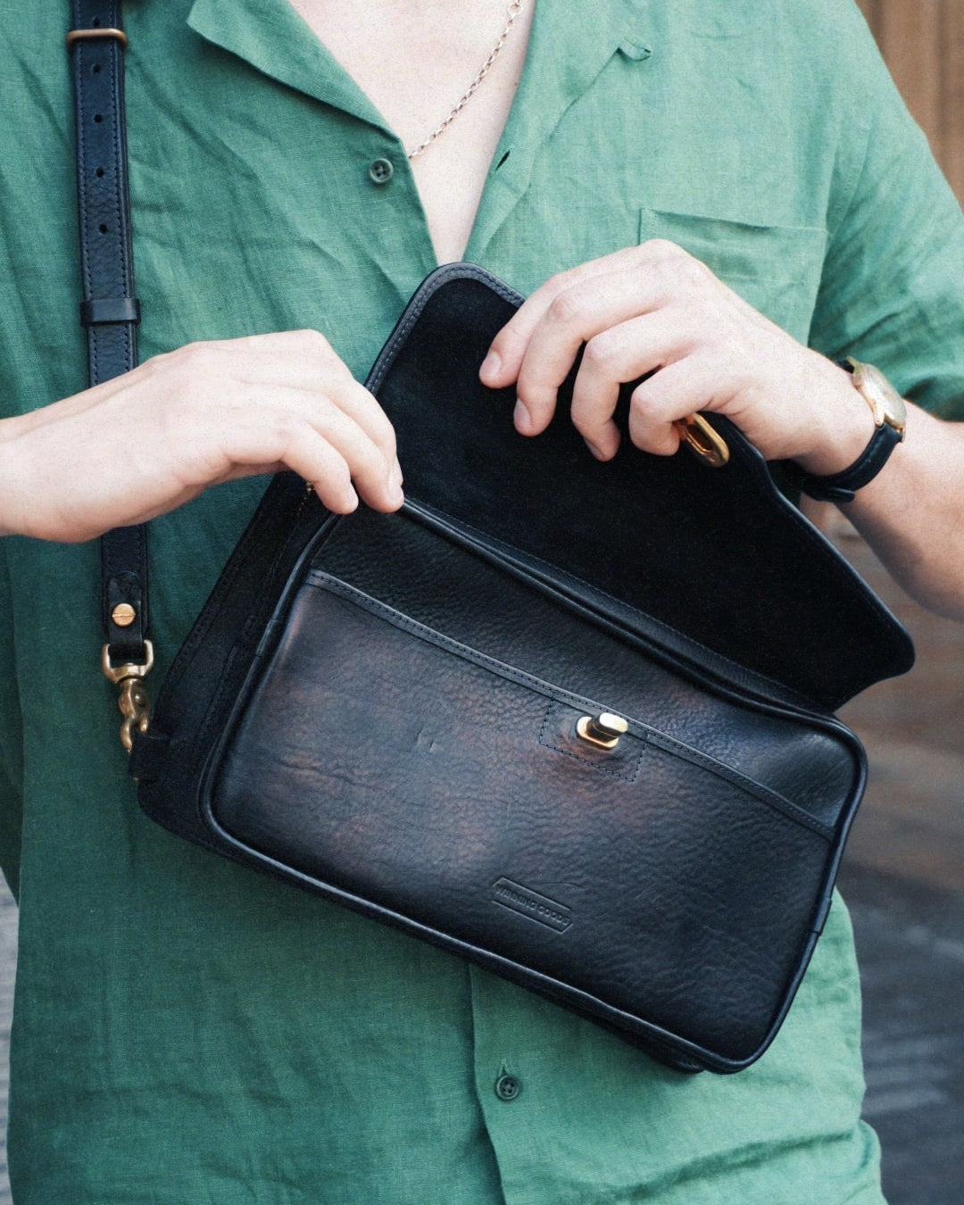 Black leather crossbosy bag with clasp and zip, being unzipped.